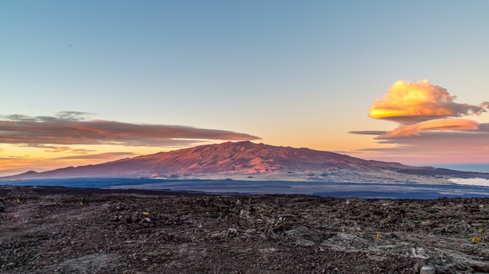 Mountain landscape at sunset with cloud formations and a rocky foreground.