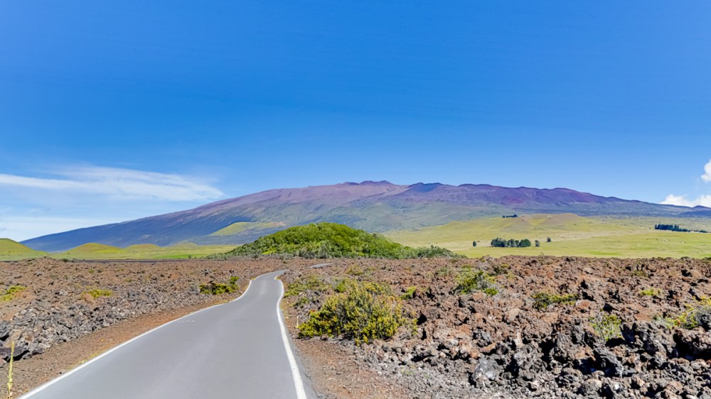 Road through volcanic landscape leading to a mountain under a clear blue sky.
